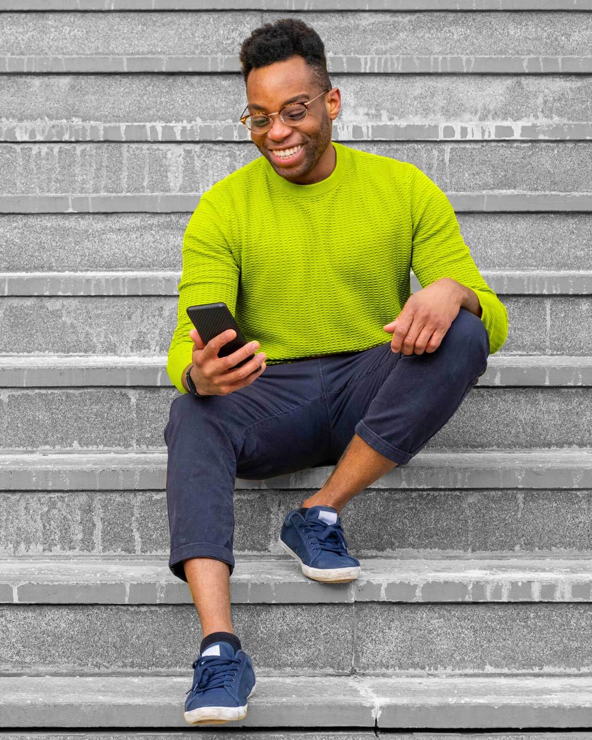 A smiling man sitting on some stairs looking at his phone