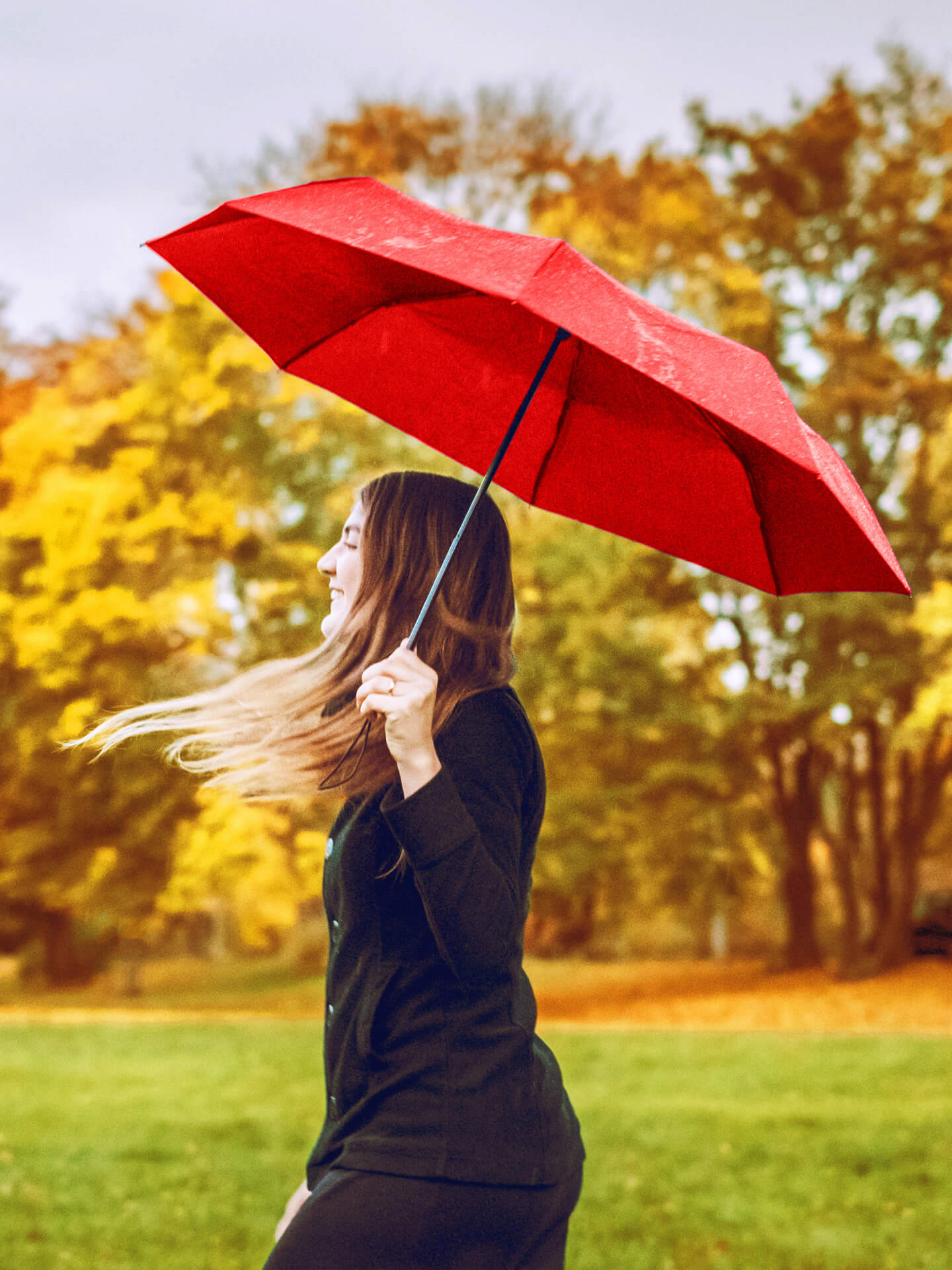A picture of a woman holding a red umbrella during what seems to be autumn