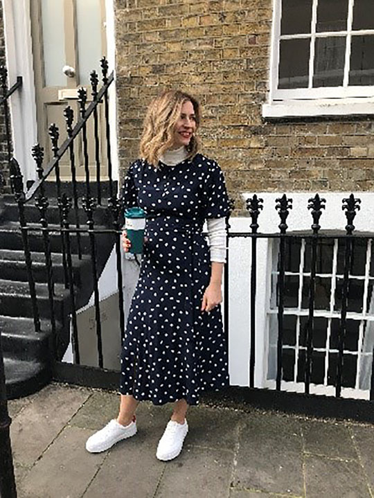 Rachel wears a white turtle neck top underneath a navy and white polka dot dress, and white trainers.