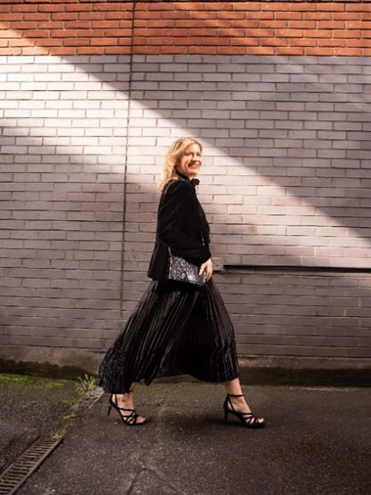 Rachel wears a black zip-through jumper, black dress and black strappy heels.