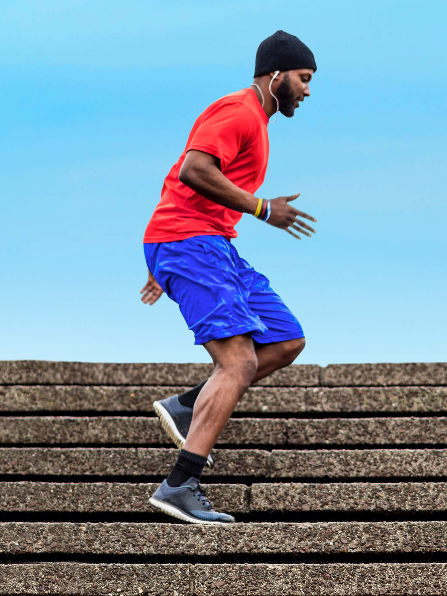 Picture of a man wearing headphones, shorts, t shirt and a beanie moving down a set of stone steps