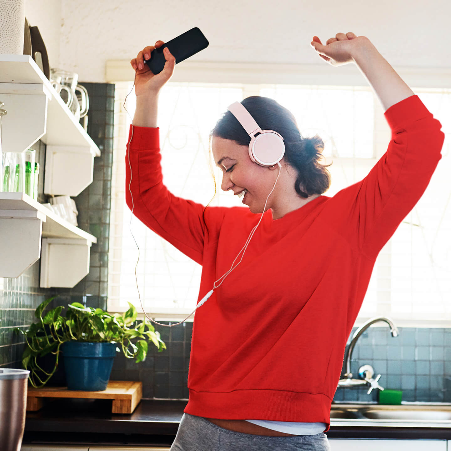 a woman dancing in her kitchen with headphones on