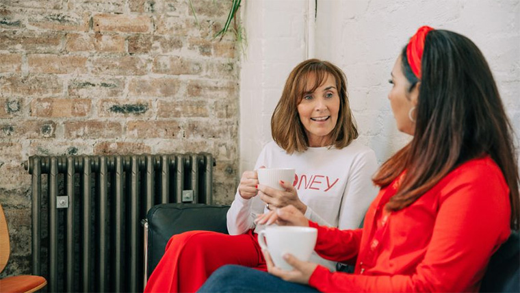 two people chatting on a sofa with a hot drink